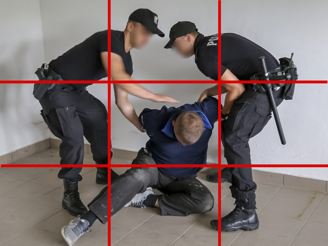 Zdjęcie wykonano w policyjnej sali ćwiczeń. Policjanci w umundurowaniu ćwiczebnym i z wyposażeniem do służby obezwładniają osobę podejrzewaną o popełnienie przestępstwa. Fotograf prawidłowo wykorzystał przestrzeń kadru. 