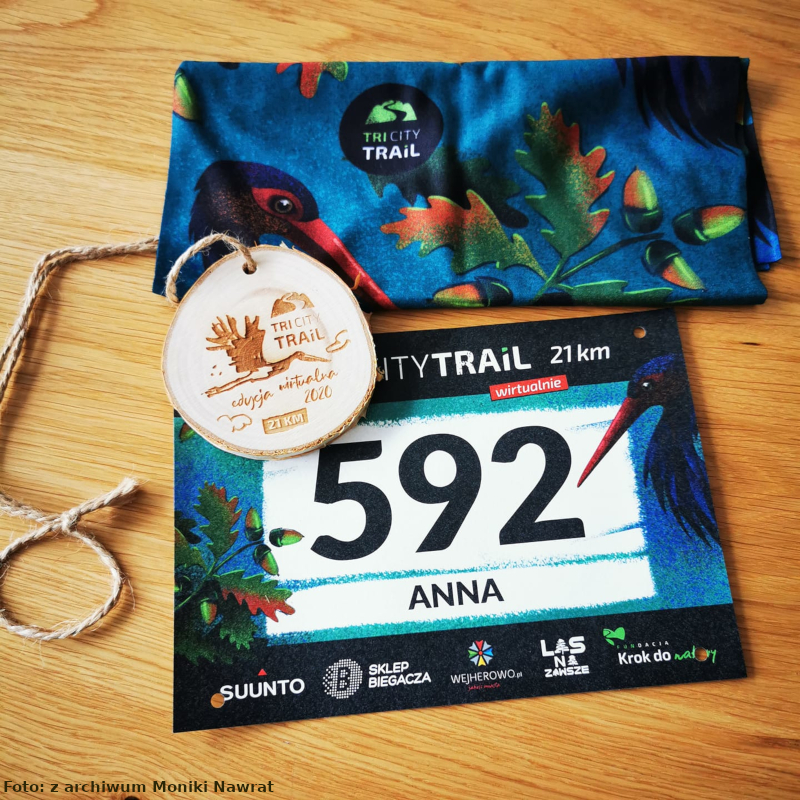 Na zdjęciu widać zestaw startowy: numer startowy, chustę, medal z logiem półmaratonu TRI CITY TRAIL.