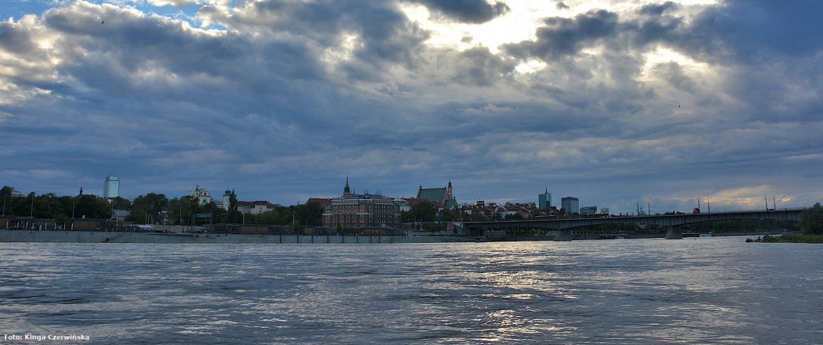 Zdjęcie przedstawia panoramę Warszawy z widokiem na most Śląsko-Dąbrowski. Na pierwszym planie widać rzekę Wisłę.