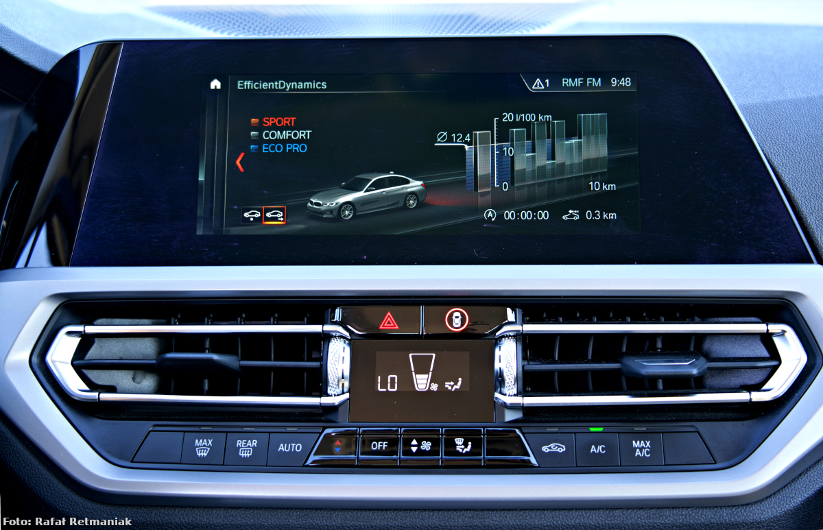 Zdjęcie wykonano w środku radiowozu marki BMW. Przedstawia wyświetlacz zamontowany w desce rozdzielczej wraz z przyciskami do obsługi m.in. klimatyzacji, stopnia nawiewu powietrza, włącznik świateł alarmowych.