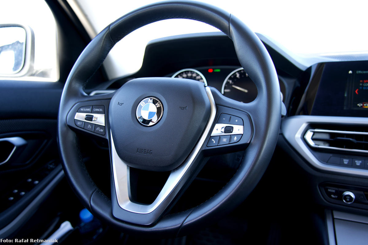 Zdjęcie wykonano w środku radiowozu marki BMW. Na pierwszym planie widać kierownicę z logiem BMW, na dalszym –  konsolę samochodową. 