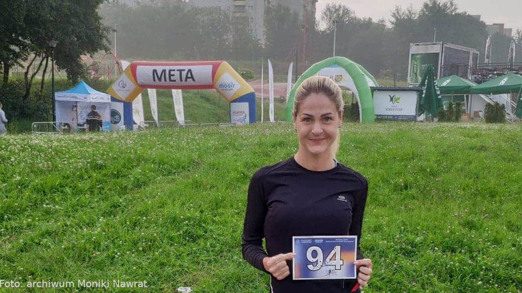 Na zdjęciu Monika Nawrat trzyma numer startowy, za nią widać metę biegu.