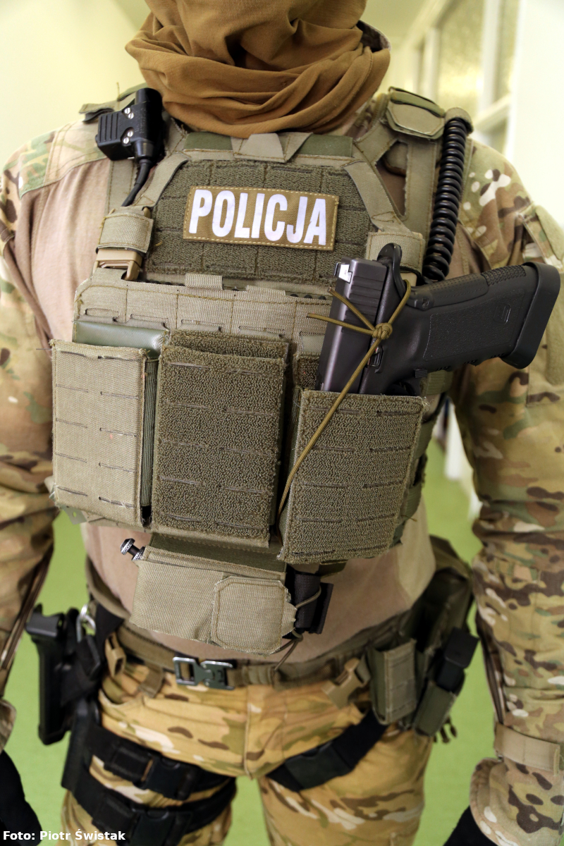 Zdjęcie przedstawia umundurowanego kontrterrorystę, który prezentuje broń mocowaną w jednej z przegródek kamizelki balistycznej.